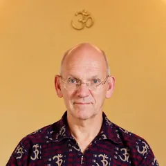 Thierry Van Brabant, assis en lotus sur un tapis de yoga dans la salle, chemise ornée de symboles Om